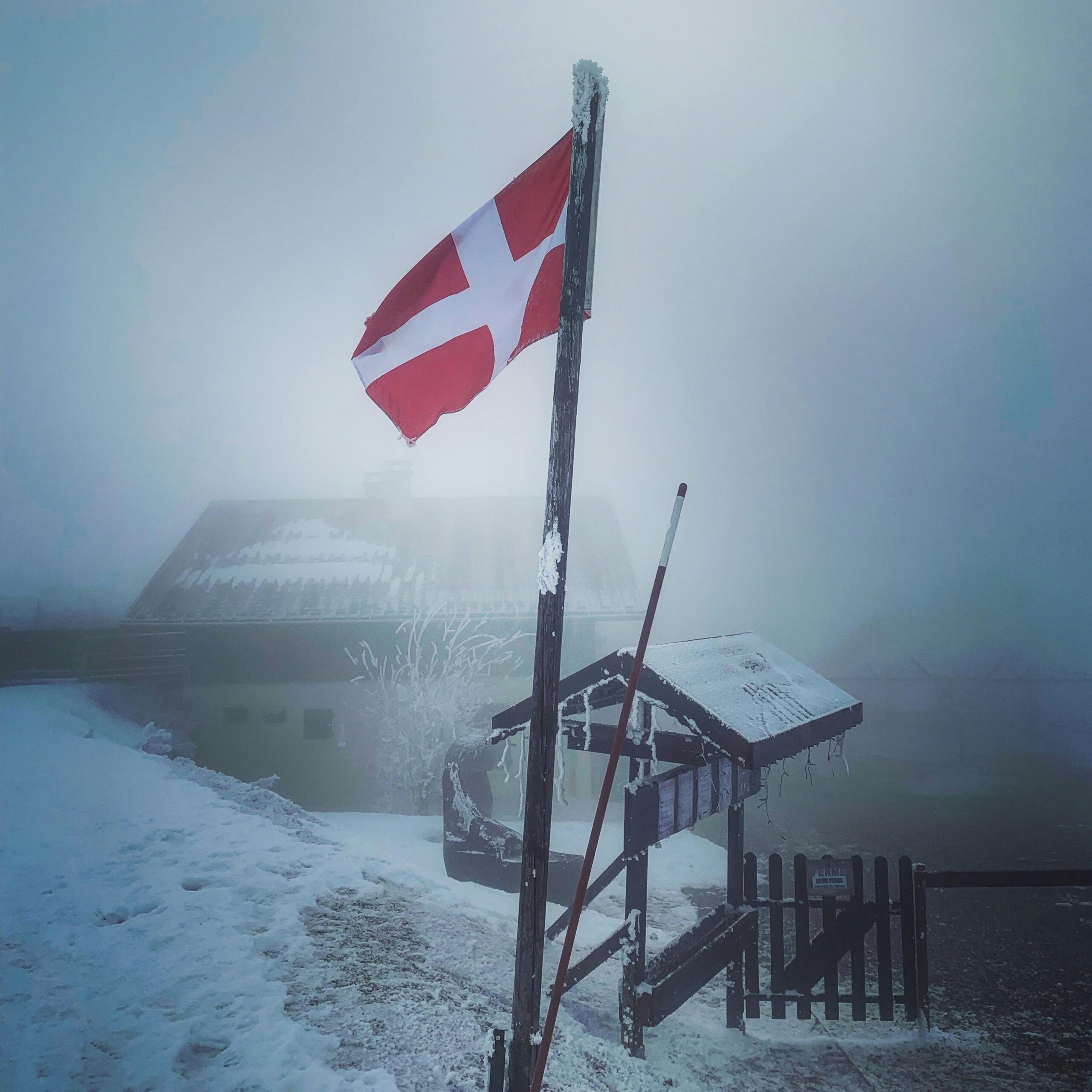 A snowy village landscape with a Danish flag, shrouded in fog, capturing a serene winter atmosphere.