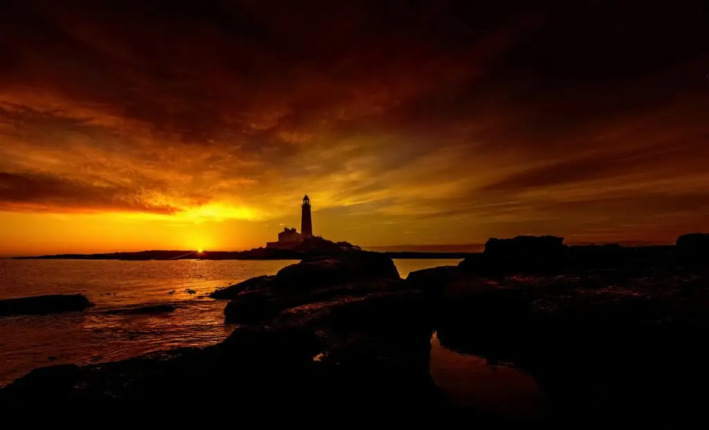 Beautiful sunset view of St Mary's Lighthouse with dramatic sky and rocky shore.