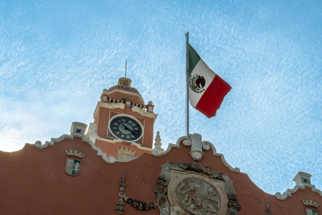 Historic clock tower of the Municipal Palace in Merida with the Mexican flag against a clear sky.