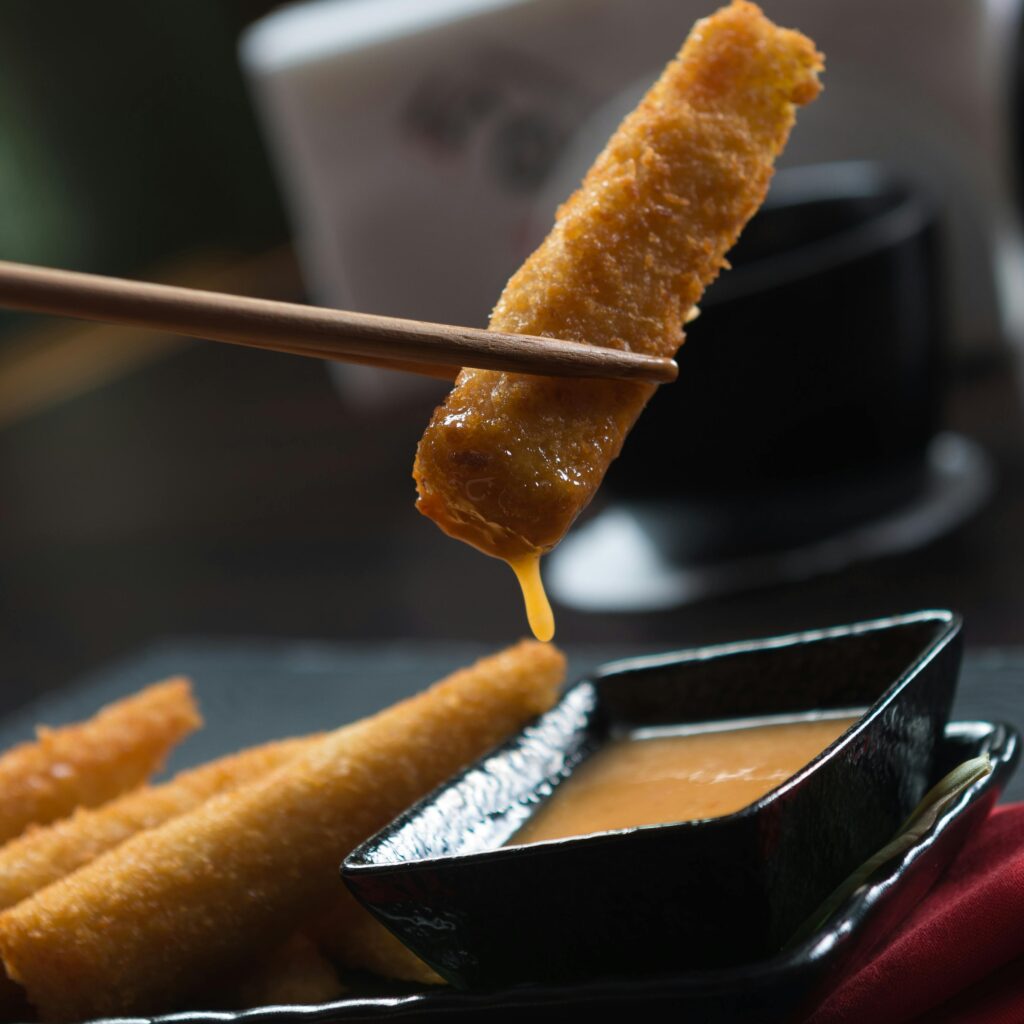 Close-up of crispy sticks being dipped in sauce with chopsticks, perfect for Asian cuisine concepts.