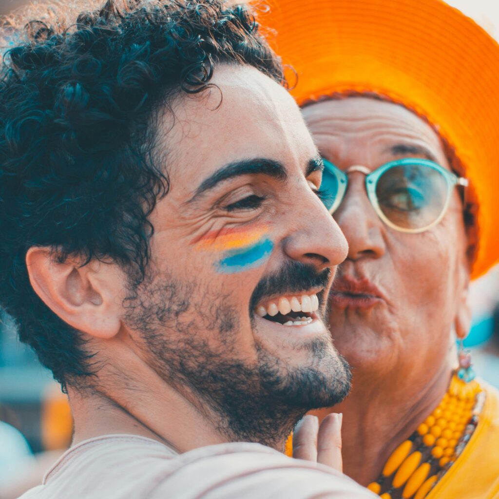 Man and older woman sharing a joyful moment with painted faces and bright attire.