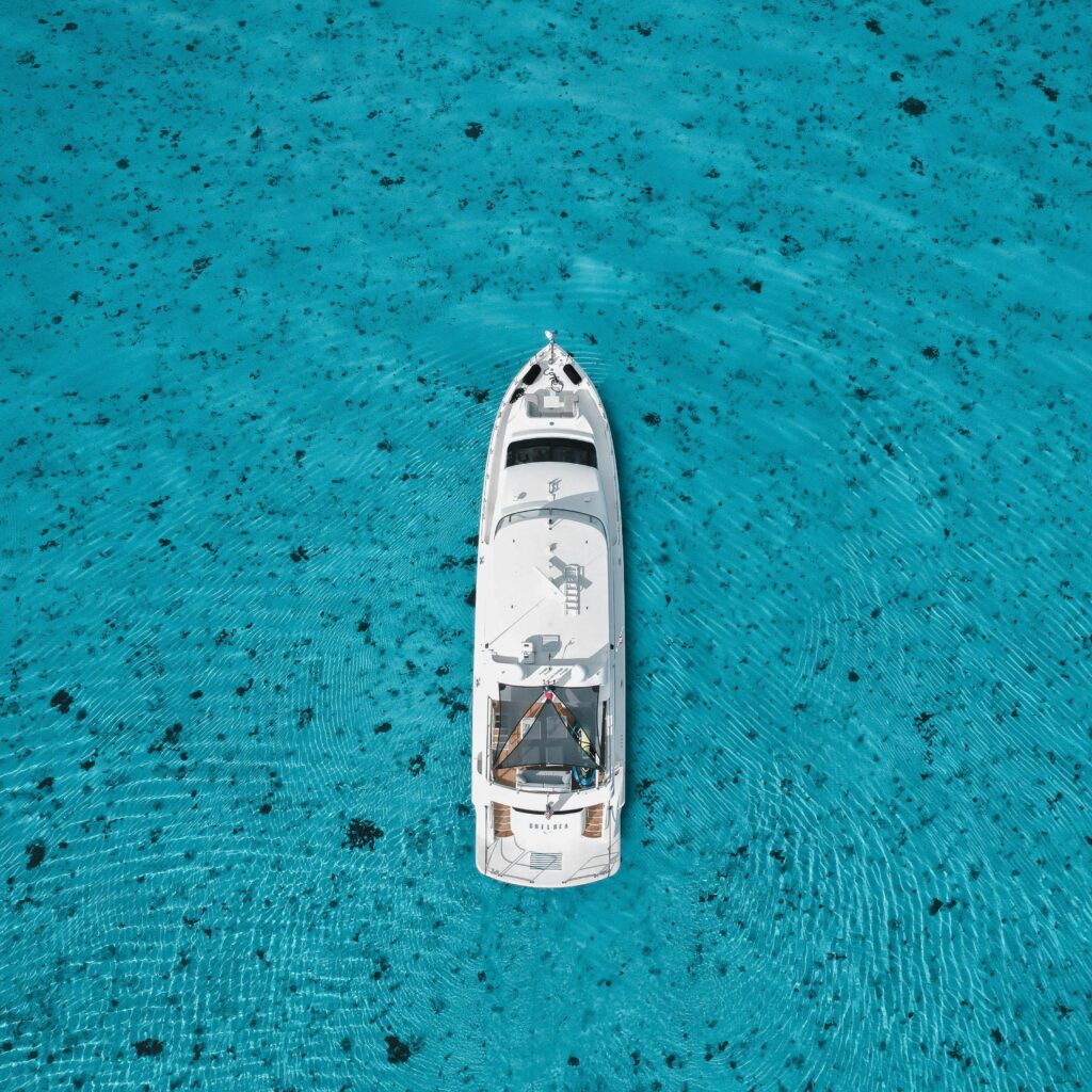 Top-down view of a white yacht in clear turquoise waters, surrounded by ripples.