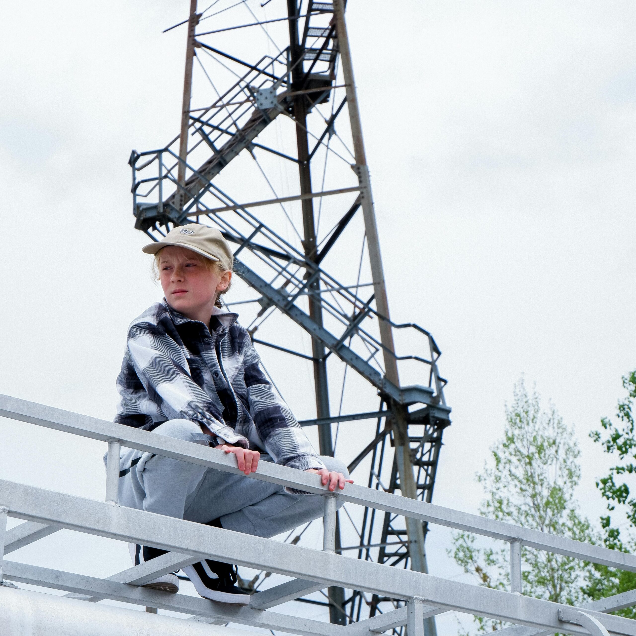 Young boy in plaid shirt sitting by metal structure on a cloudy day.
