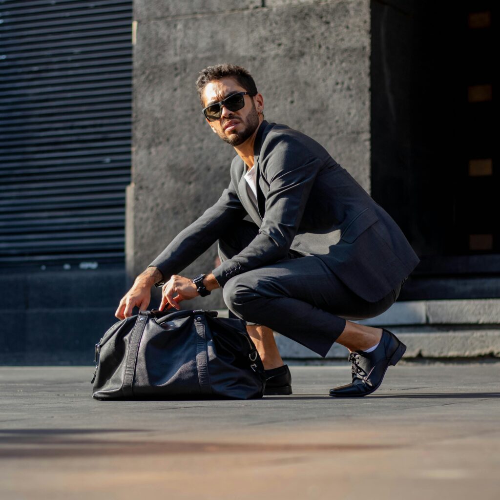 A fashionable man crouches with a bag on the streets of Mexico City.