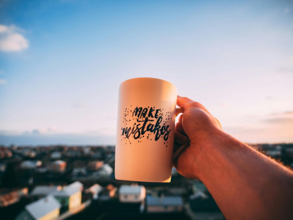 A hand holding a motivational mug with 'Make Mistakes' against a sunset in Lviv.
