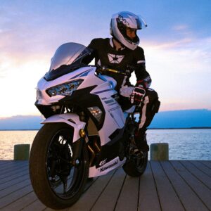 Motorcyclist in gear poses by a picturesque sunset lake, showcasing a sleek Kawasaki bike.