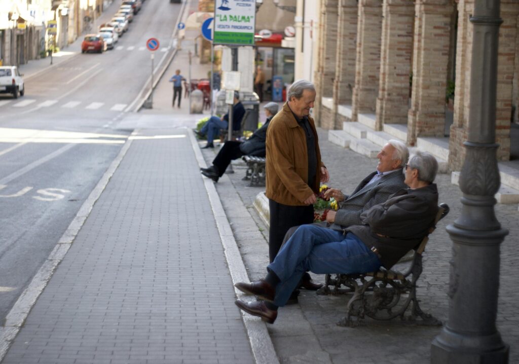 Elderly men enjoying a relaxed discussion on a quaint street in Loreto, Italy.