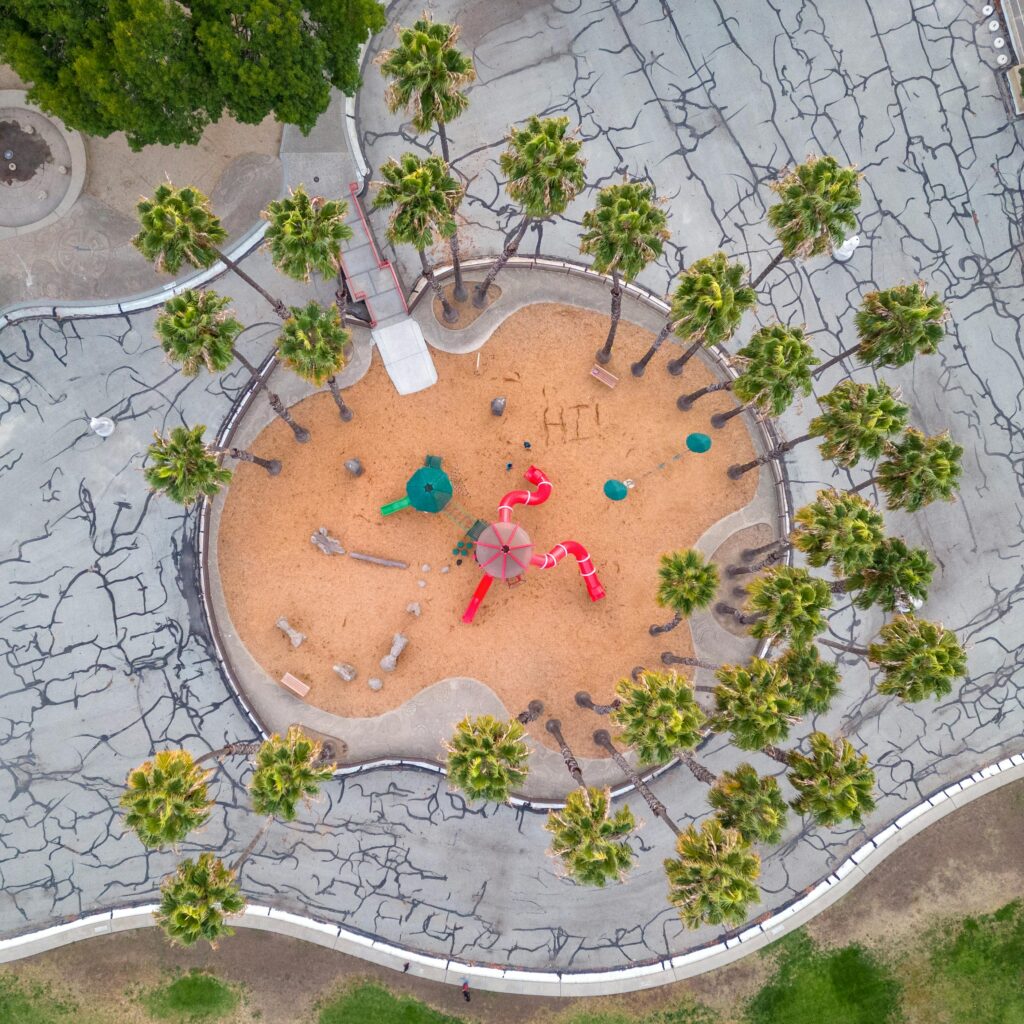 Aerial view of a circular playground with palm trees and play equipment in a park.