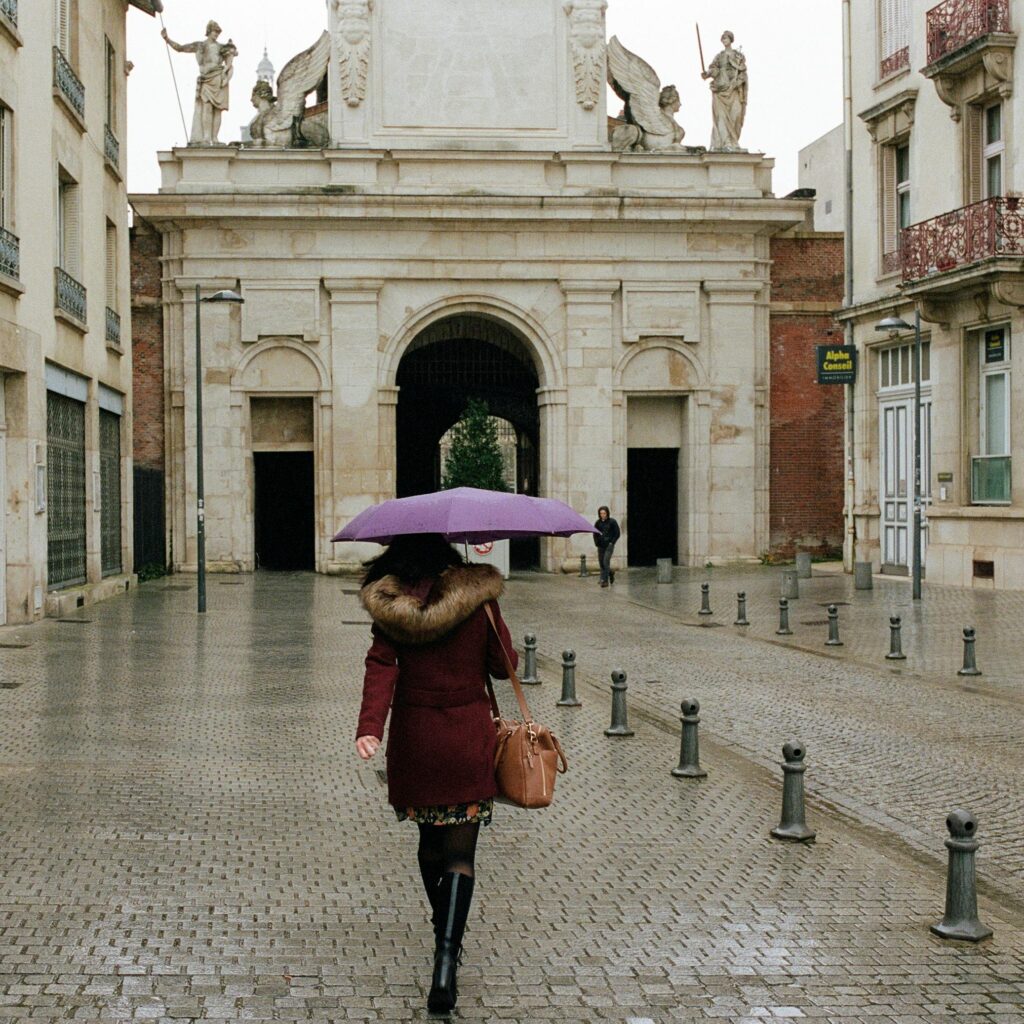 A woman in a coat walks with an umbrella on a rainy day in Nancy, France.