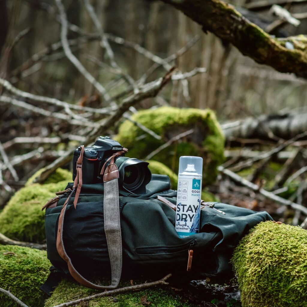 Camera and waterproof spray on a backpack in a mossy forest setting, perfect for outdoor photography enthusiasts.