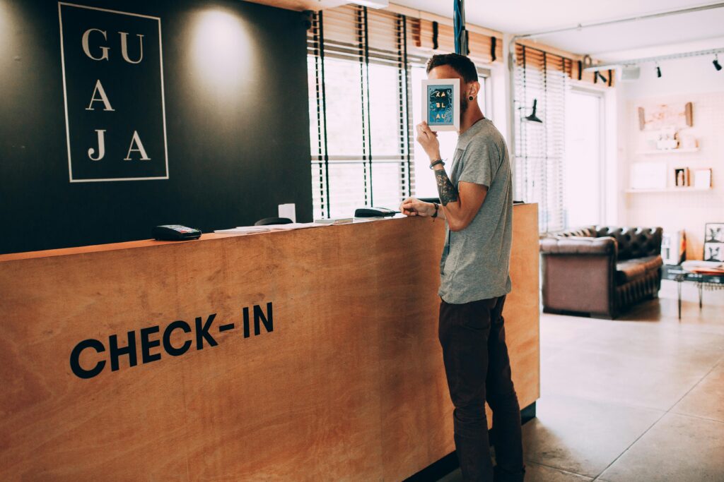 Man standing at a reception desk, holding a book, in a modern hotel lobby.
