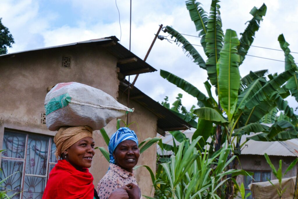 Smiling women in Arusha, Tanzania carrying a sack over traditional attire in a village setting.