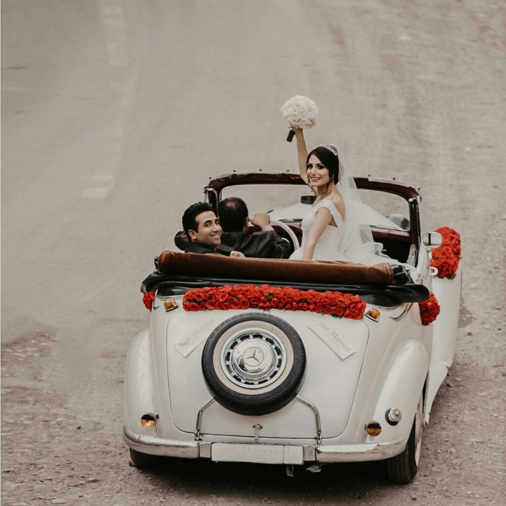 A newlywed couple celebrates their wedding in a vintage convertible adorned with roses, driving into a new future.