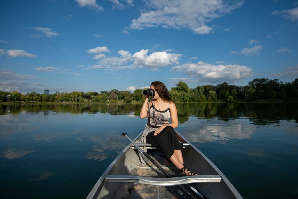 Young woman capturing scenic lake views with a camera from a boat under a clear blue sky.