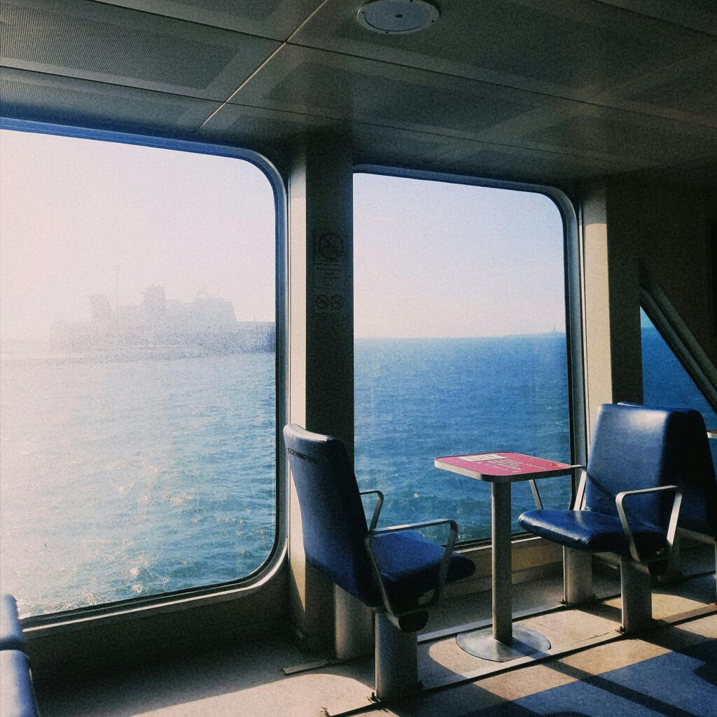 Interior view of an empty ferry with ocean scenery through large windows, capturing a peaceful and nostalgic travel moment.