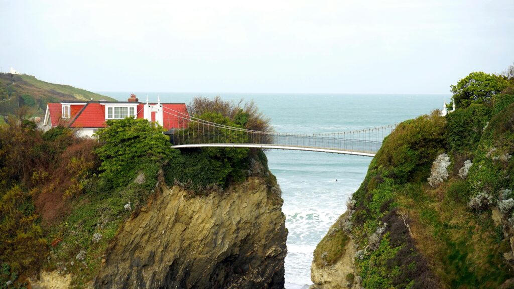 A picturesque house on a cliff in Cornwall connected by a unique bridge, overlooking the sea.