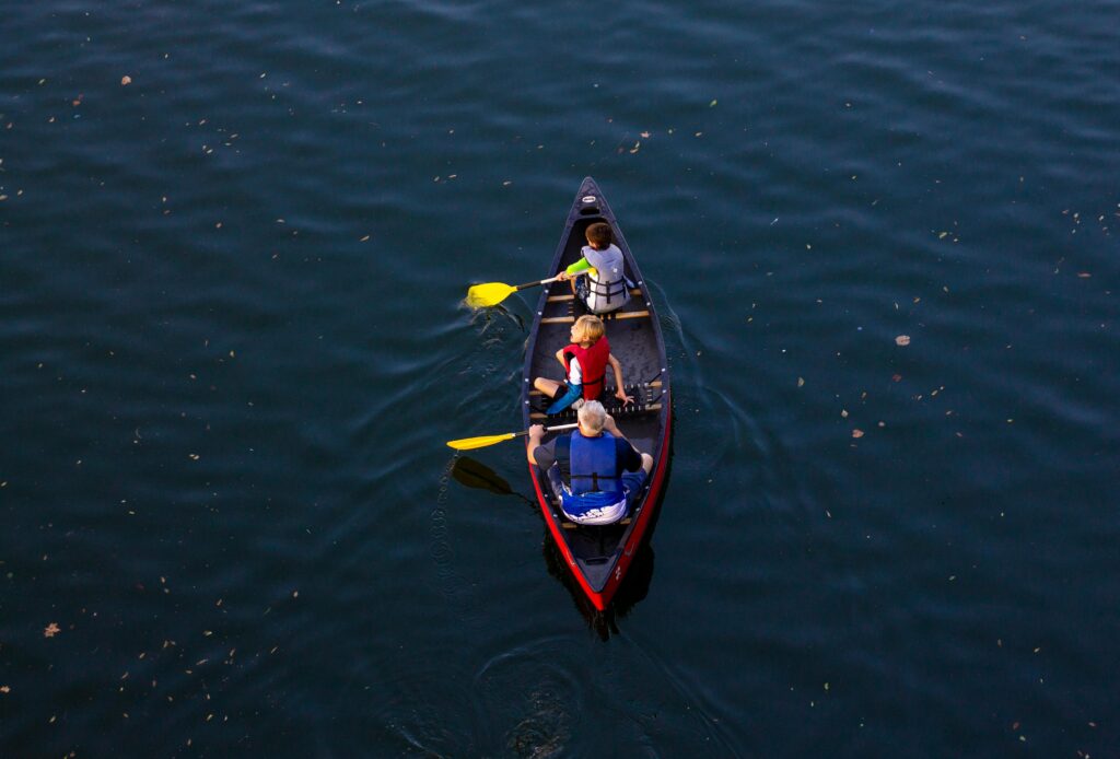Grandparent and grandchildren enjoying a canoe ride on a serene lake under the sun.