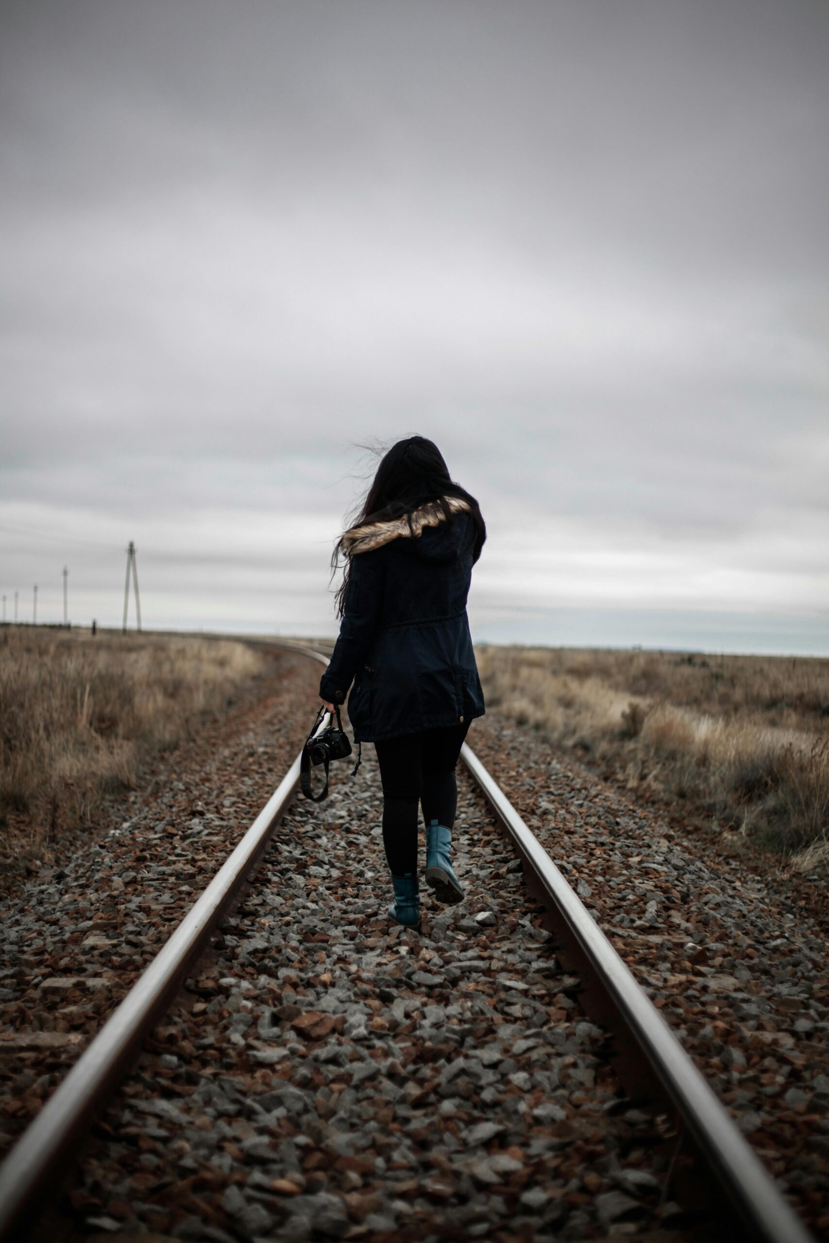 Rear view of a woman walking alone on railway tracks during twilight, conveying solitude and journey.