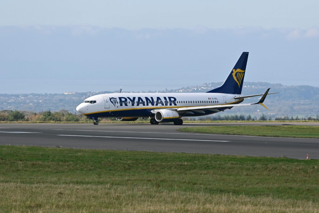 A Ryanair aircraft on the runway preparing for takeoff with a scenic backdrop of distant hills and clear skies.