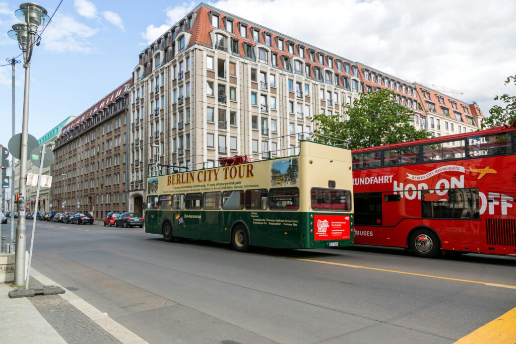 Double-decker tour buses drive through a Berlin street, offering city sightseeing.