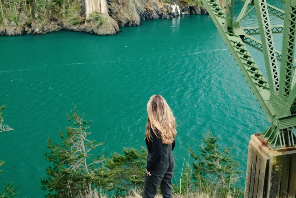 Woman overlooking serene ocean from a rocky, green cliff. Perfect travel inspiration.