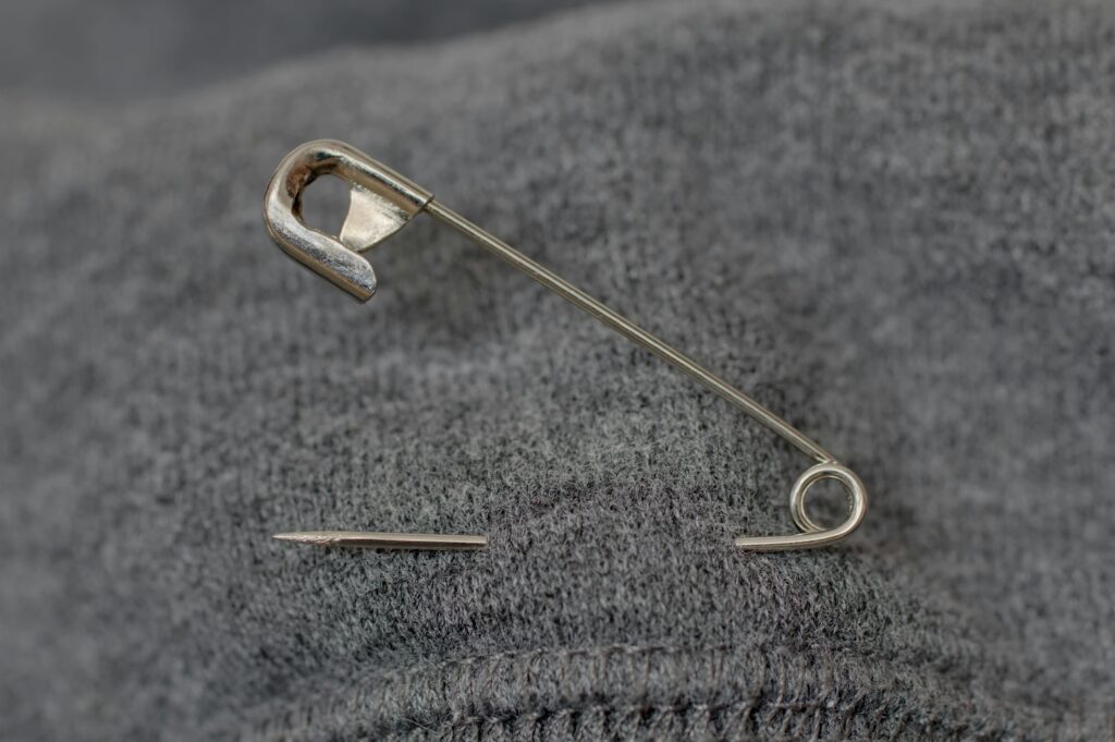 A detailed view of a safety pin resting on a textured gray fabric surface.
