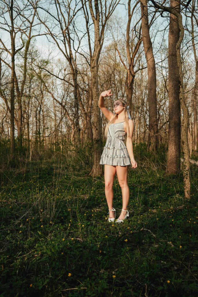 A young woman in a light dress poses in a vibrant spring forest with bare trees.