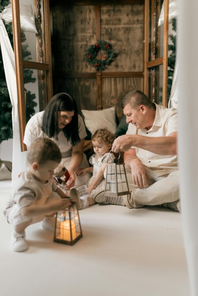 A family with young children sharing a warm moment indoors, holding lanterns in a cozy winter setting.