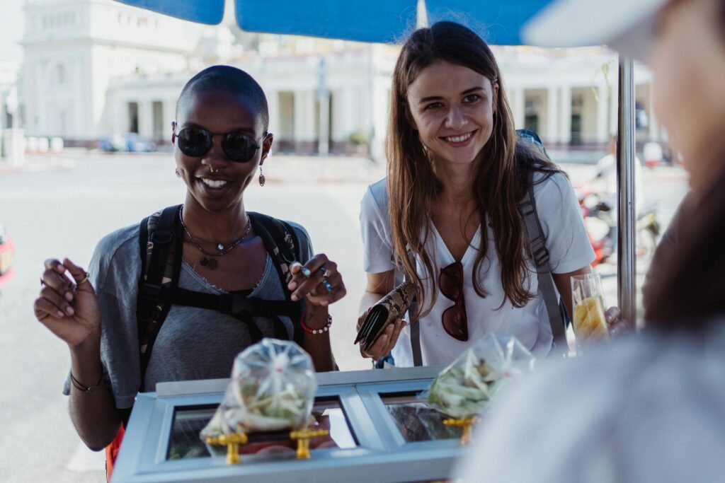 Two women enjoying street food at an outdoor market, exuding joy and travel spirit.