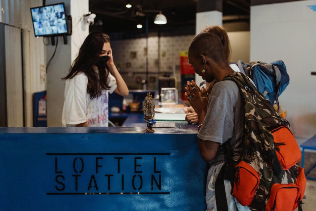 Travelers checking in at a hostel reception desk in a lively urban setting.
