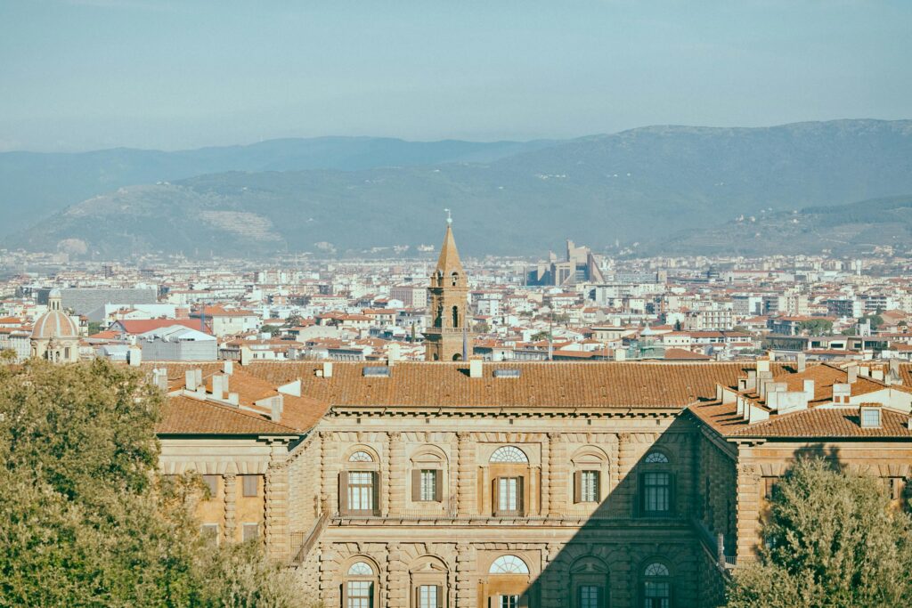 Facade of aged stone house near trees against old city with residential buildings and mountainous area