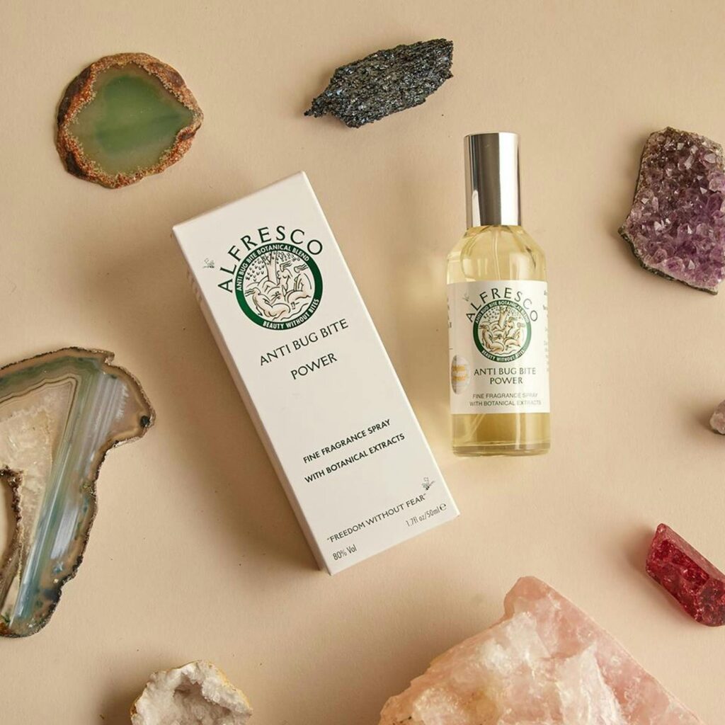 Flat lay of Alfresco anti bug bite spray and box with gemstones on beige background.