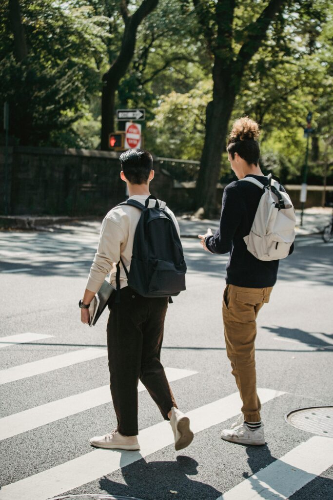 Young men with backpacks crossing a city street during a sunny day, showcasing urban lifestyle and friendship.