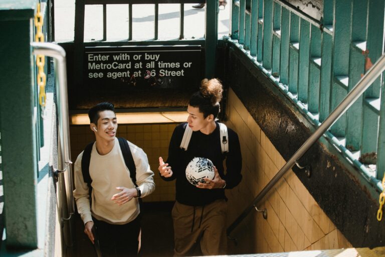 Two young men chatting as they exit a subway in New York City, one carrying a soccer ball.