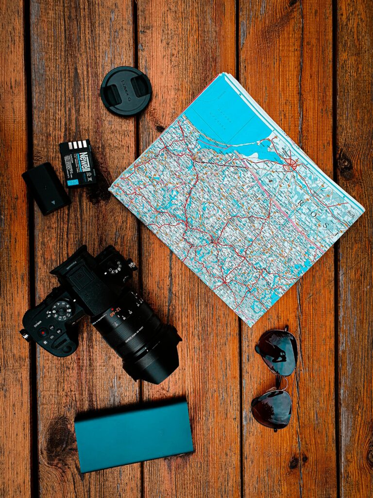 pexels-photo-5798941-5798941 Flat lay of travel gear including camera, map, and sunglasses on wooden surface.