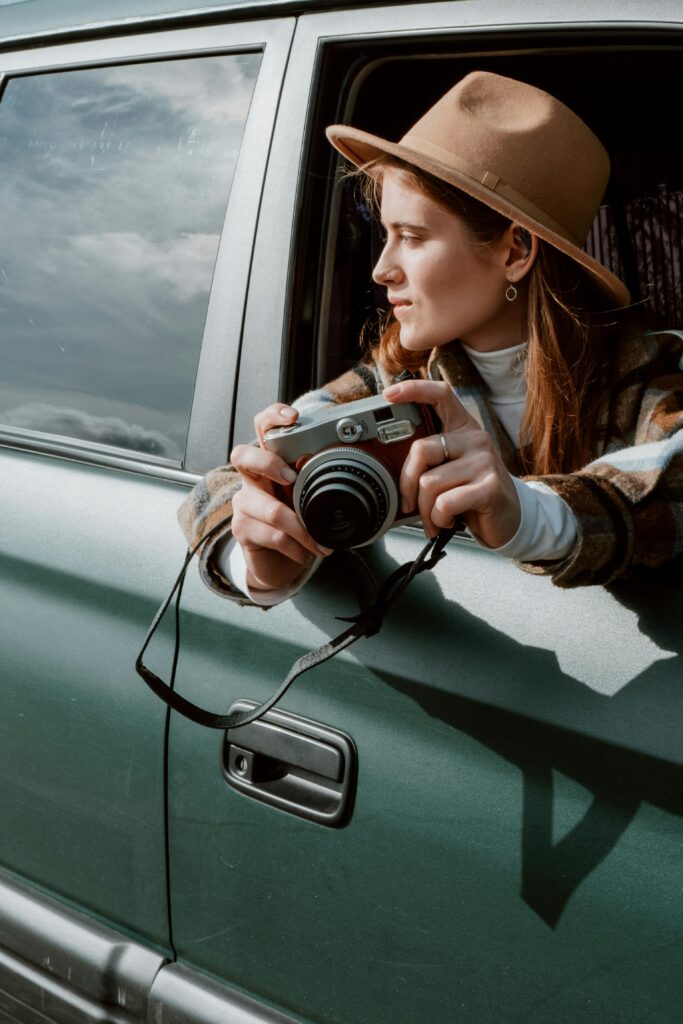 A woman with a vintage camera captures moments from a car window on a road trip.