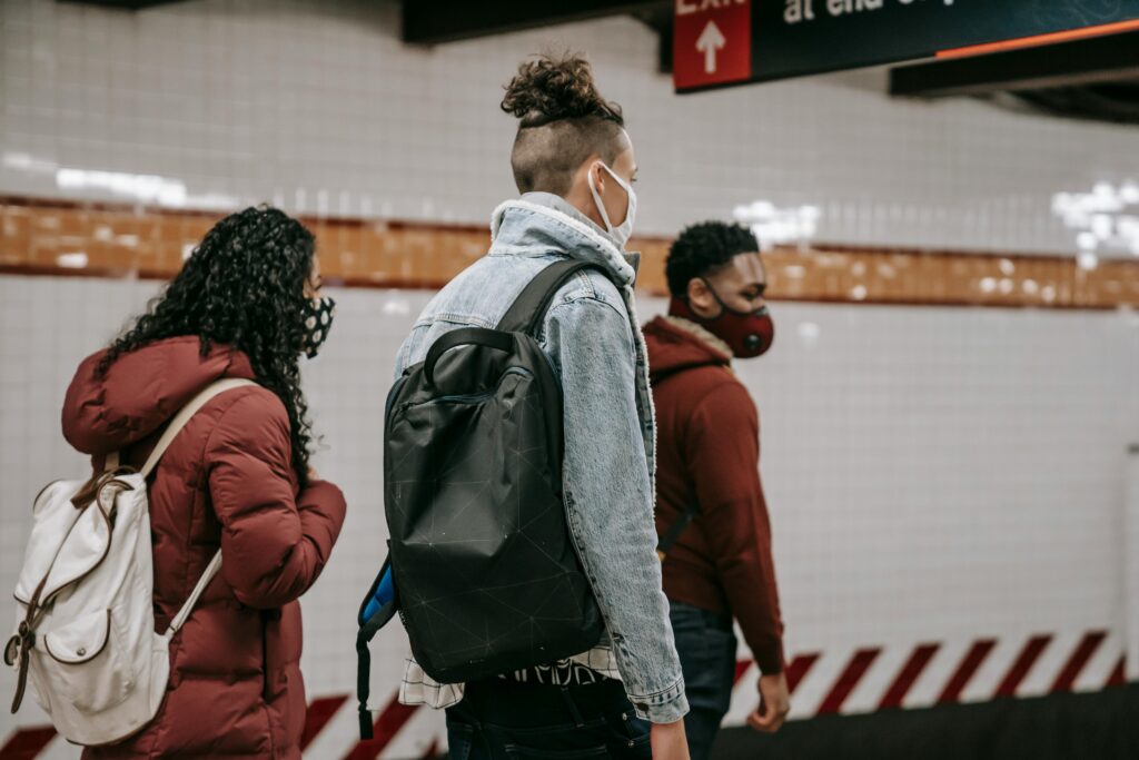 Side view of anonymous young multiracial friends in warm clothes and protective masks with backpacks walking on underground station
