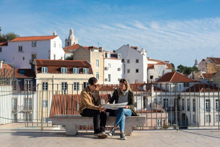 A couple sitting on a bench looking at a map with Lisbon's rooftops in the background.