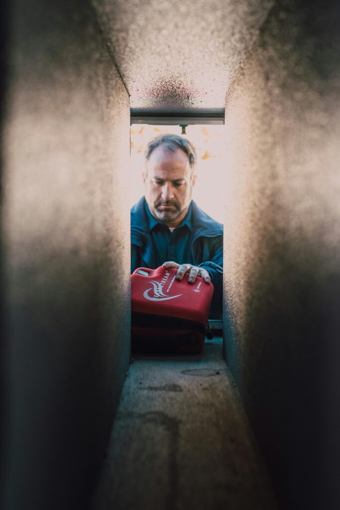 A paramedic placing a red medical kit inside a locker, symbolizing readiness and emergency response.