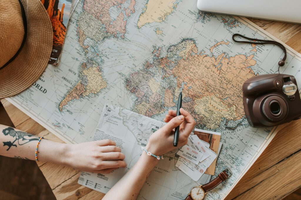 pexels-photo-7368300-7368300 Top view of a woman's hands planning a trip with a map, camera, and travel items.