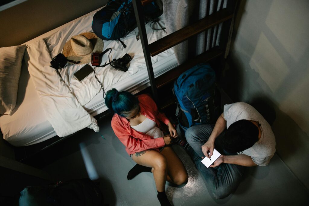 A young couple using a smartphone in a hostel room with backpacks, ready for travel.