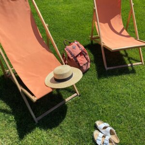 Two comfortable beach chairs with a backpack, sandals, and sunhat on a sunny day.