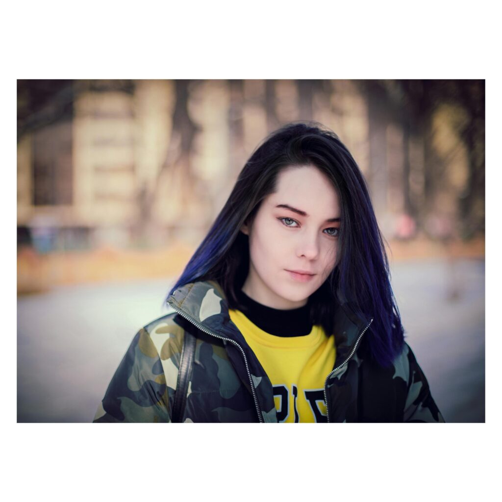 Close-up portrait of a young woman with blue hair in a stylish jacket on a fall day in Almaty.