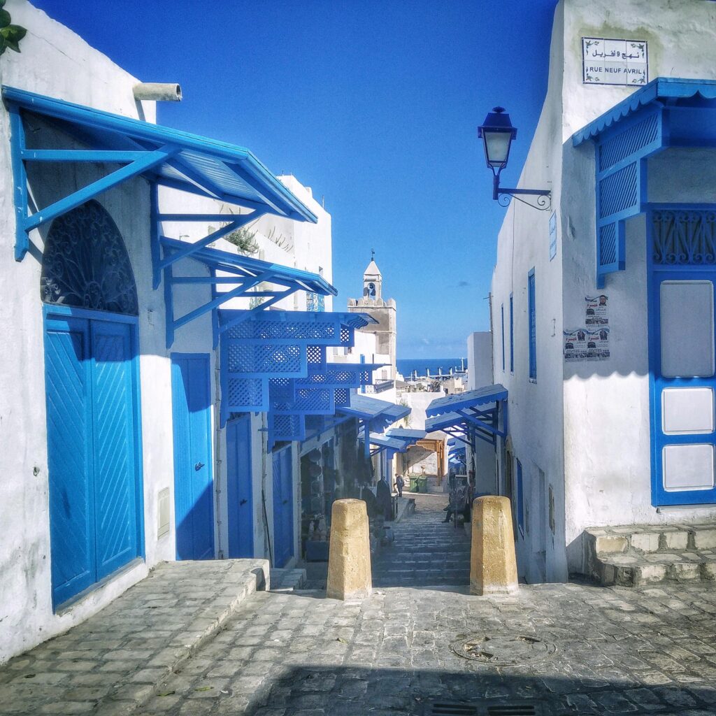 Narrow cobblestone street with iconic blue and white architecture in Sousse, Tunisia, under a clear blue sky.