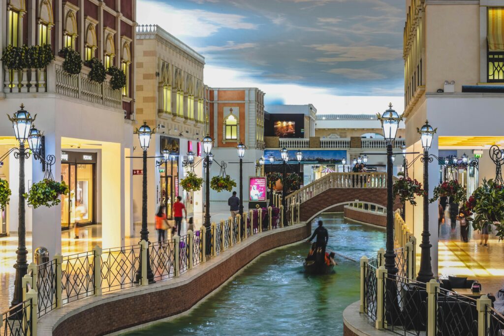 A vibrant indoor shopping mall featuring a Venetian-style canal with gondolas and storefronts.