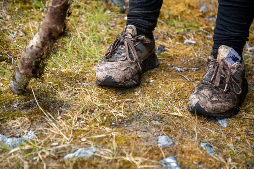Close-up of worn hiking sneakers on a muddy trail in Southland, New Zealand.