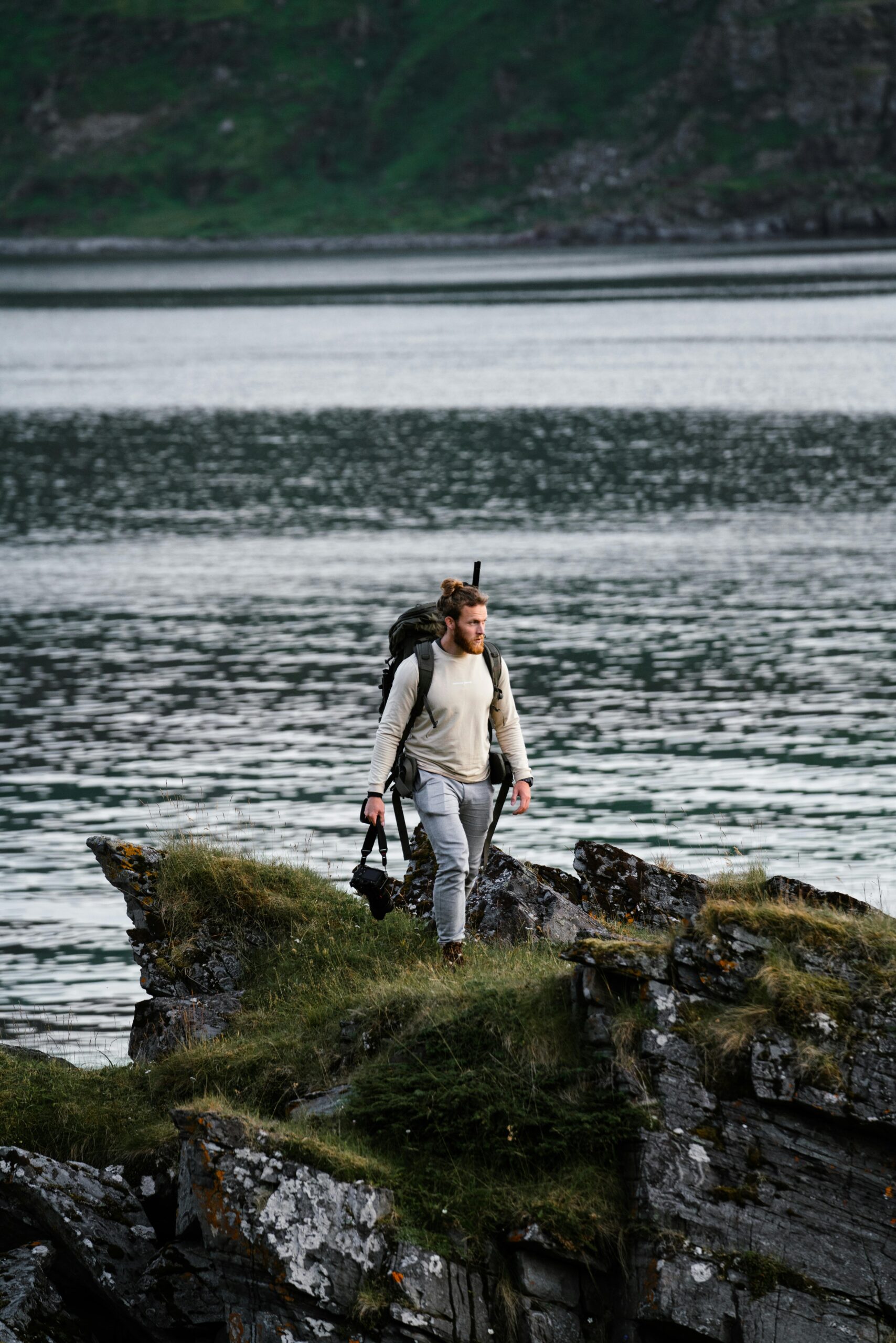 A man explores a rocky cliffside by a fjord in Norway, capturing the rugged beauty of Troms og Finnmark.