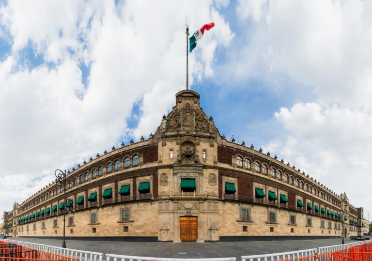Panoramic view of the National Palace, Mexico City, with a Mexican flag under a cloudy sky.