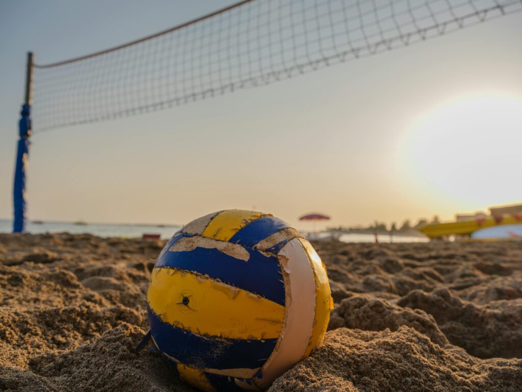 A volleyball rests on a sandy beach near a net during a beautiful sunset.