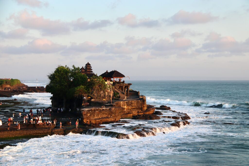 Scenic aerial view of the iconic Tanah Lot Temple on the coast of Bali, surrounded by waves.